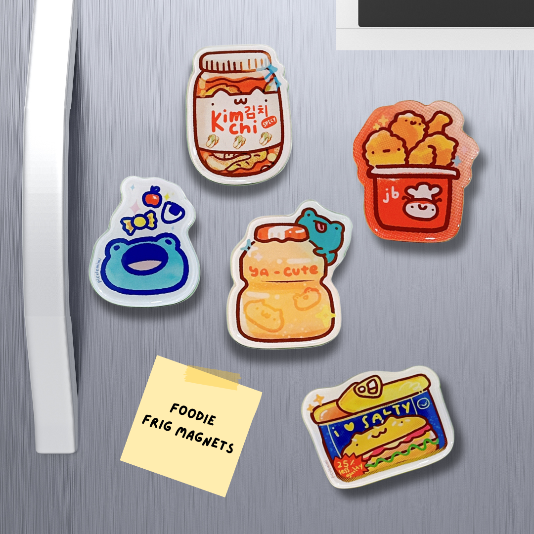 Set of colorful refrigerator magnets on a metallic surface with a note labeled 'Foodie Frig Magnets'.