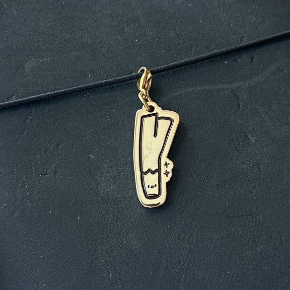 A black leather journal with a wrap-around strap and a small gold metal charm, held by a hand over a light wood floor background.