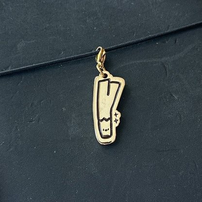 A black leather journal with a wrap-around strap and a small gold metal charm, held by a hand over a light wood floor background.