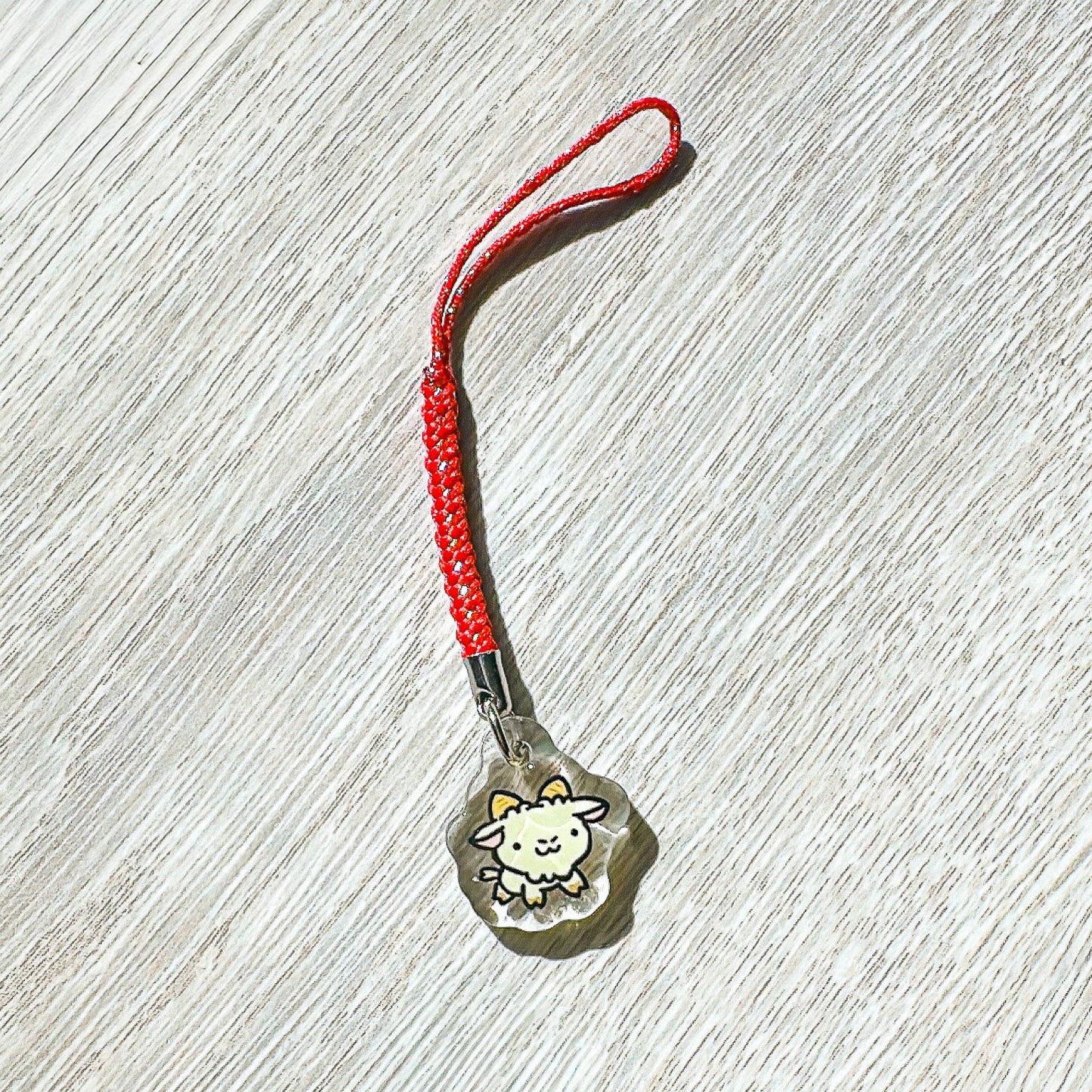 Small  year of the sheep charm with a red string on a wooden surface