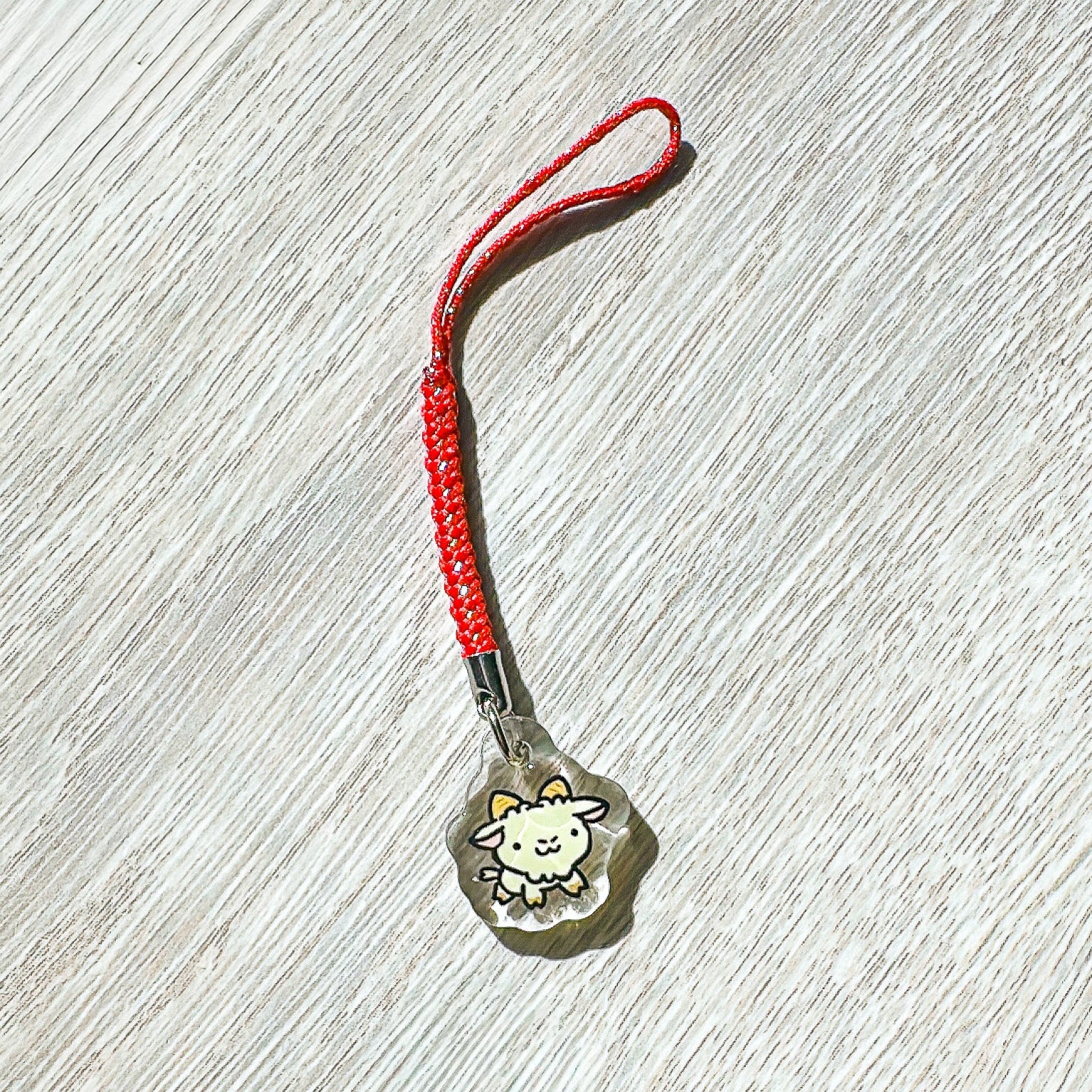 Small  year of the sheep charm with a red string on a wooden surface