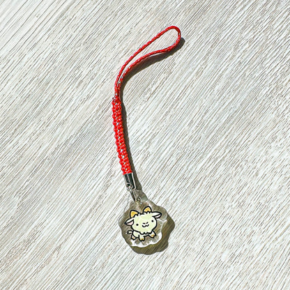 Small  year of the sheep charm with a red string on a wooden surface