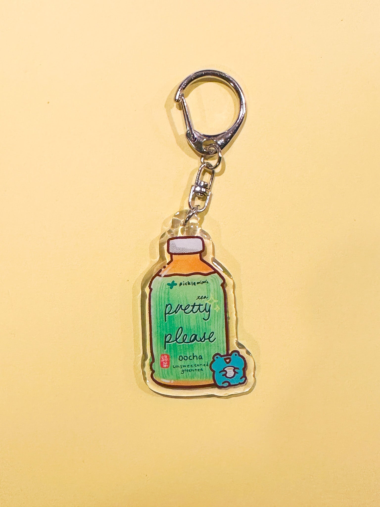 Keychain with green tea bottle and frog design on a yellow background