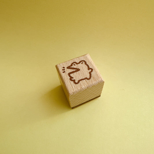 A small wooden cube stamp with a brown engraved outline of a duck, set against a solid pale yellow background.