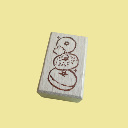 A rectangular wooden rubber stamp with a brown etched design of stacked donuts, shown on a light green background.