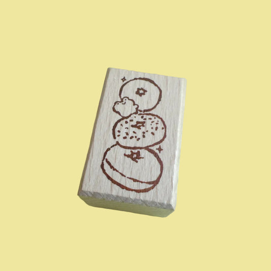 A rectangular wooden rubber stamp with a brown etched design of stacked donuts, shown on a light green background.