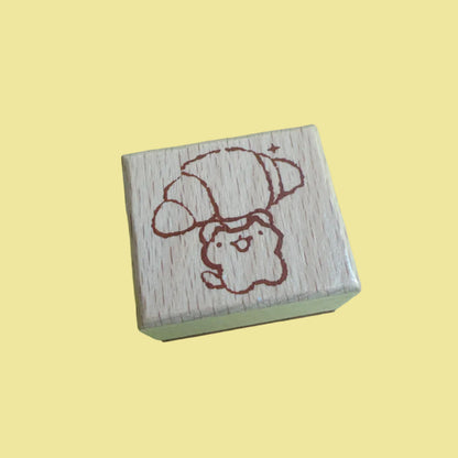 A small wooden rubber stamp with a cute cartoon dog wearing a hat, shown on a light green background.
